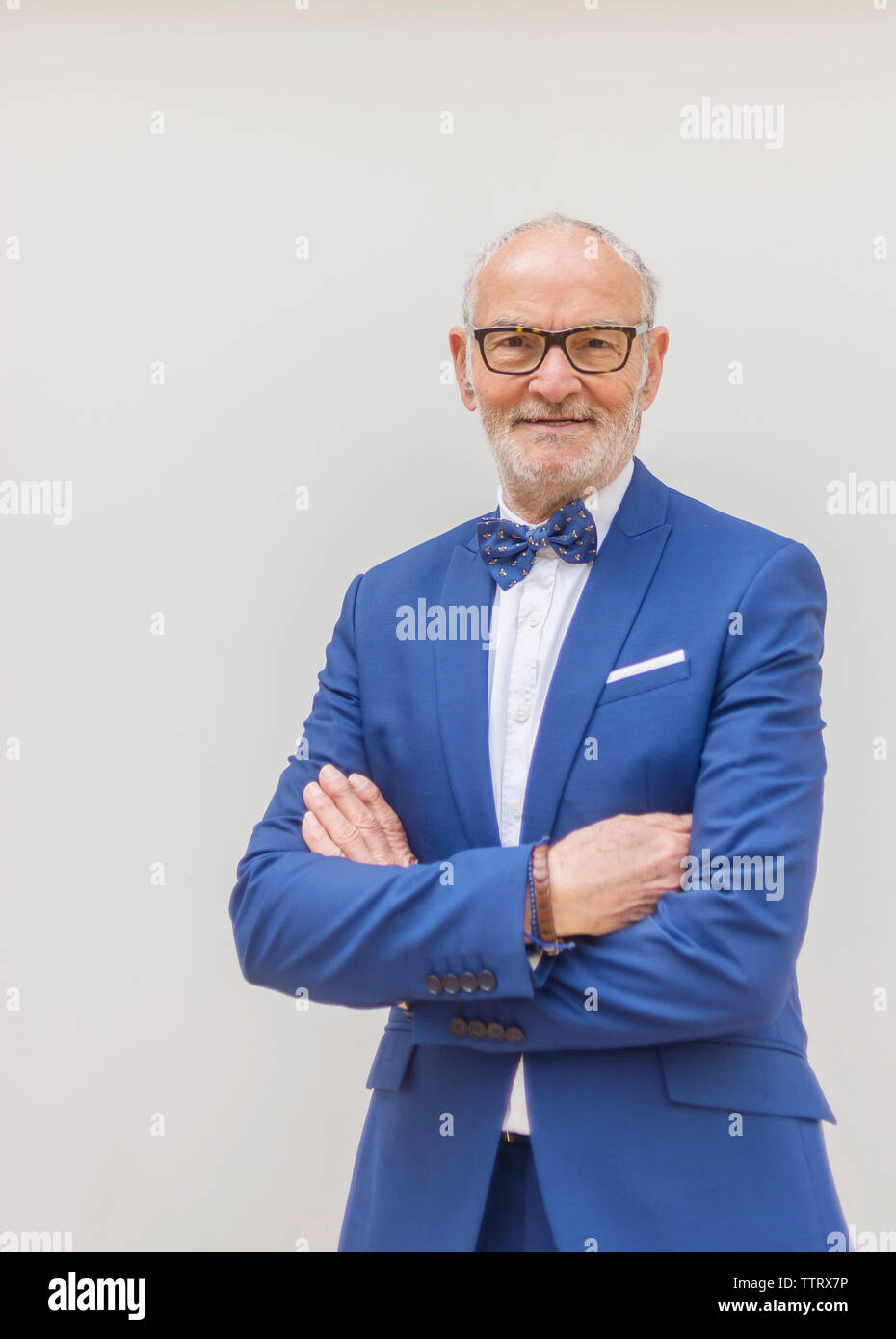Ritratto di sorridere senior uomo in tuta con le braccia incrociate in piedi contro uno sfondo bianco Foto Stock