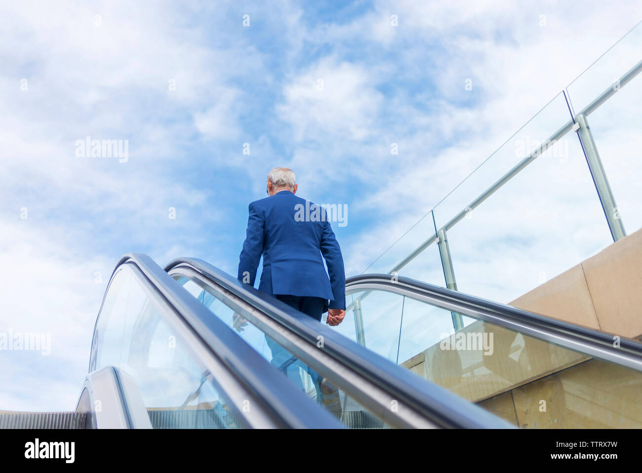 Vista posteriore del senior uomo in tuta in piedi sulla scala mobile contro il cielo nuvoloso Foto Stock
