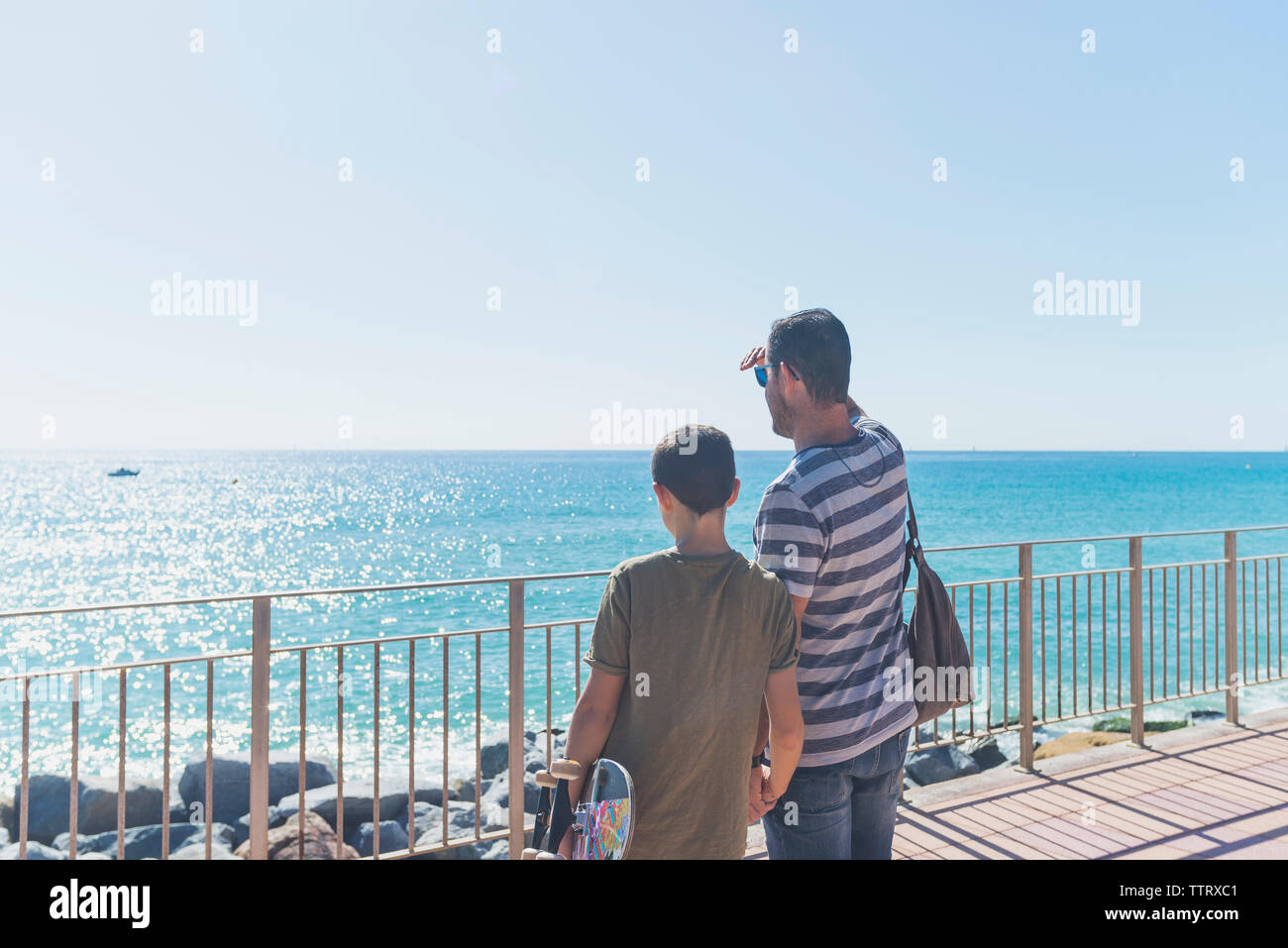 Vista posteriore del figlio e del padre che guarda lontano mentre si sta in piedi sul mare Foto Stock