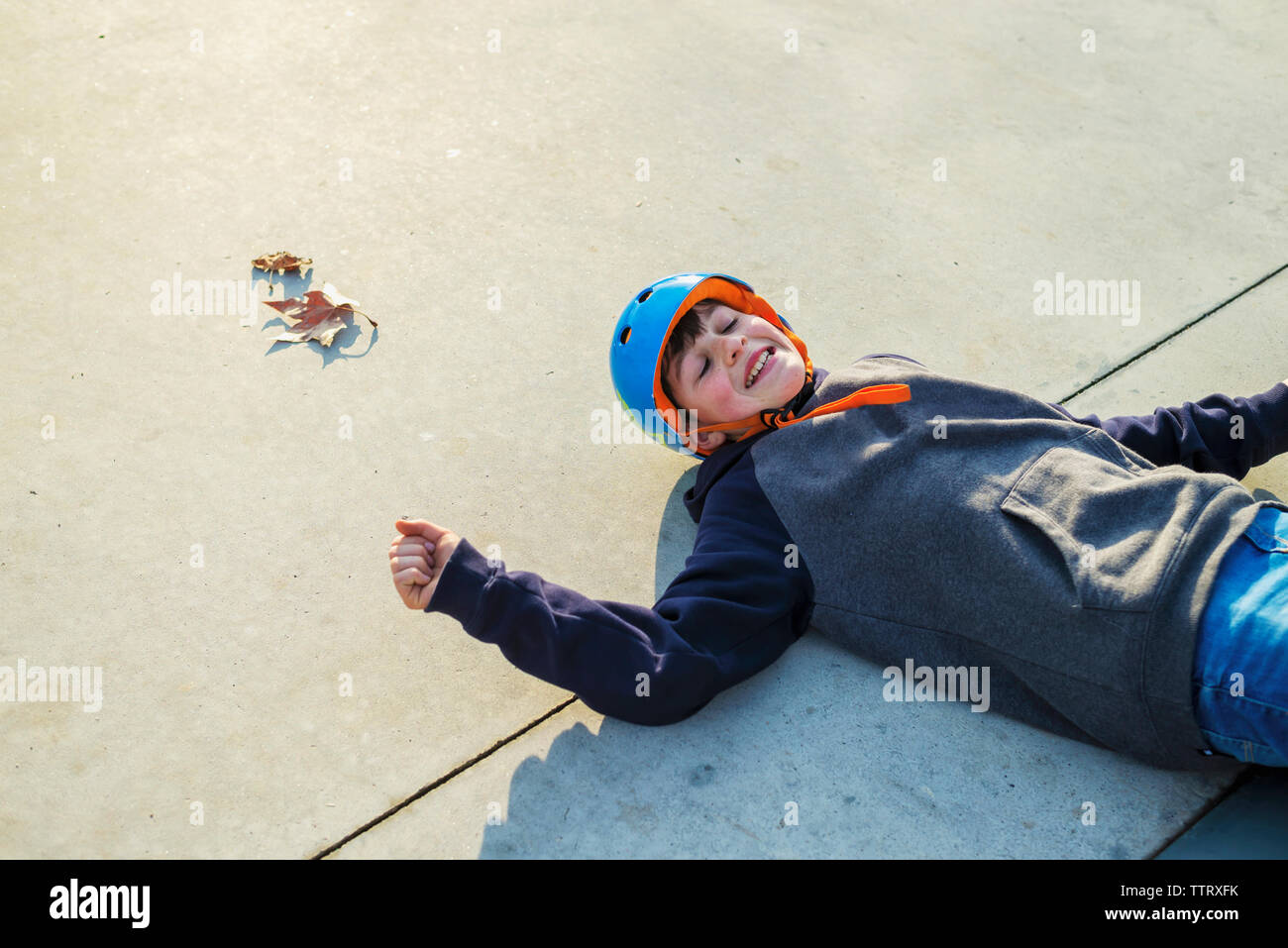 Al di sopra di vista del giovane pattinatore indossa il casco blu che giace a terra sorridente Foto Stock