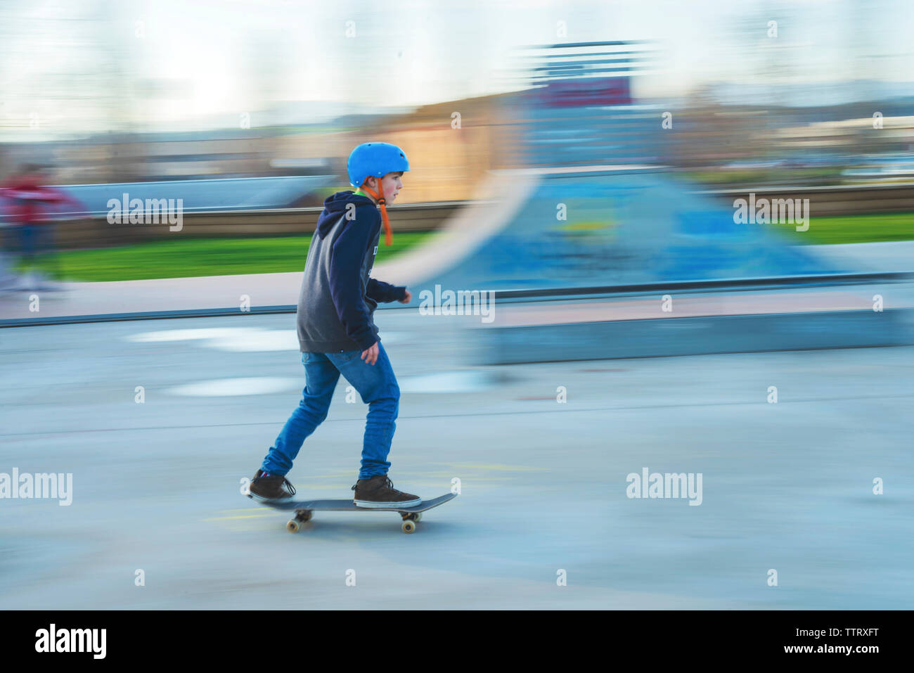 Vista laterale del giovane pattinatore indossa il casco blu in movimento a skatepark Foto Stock