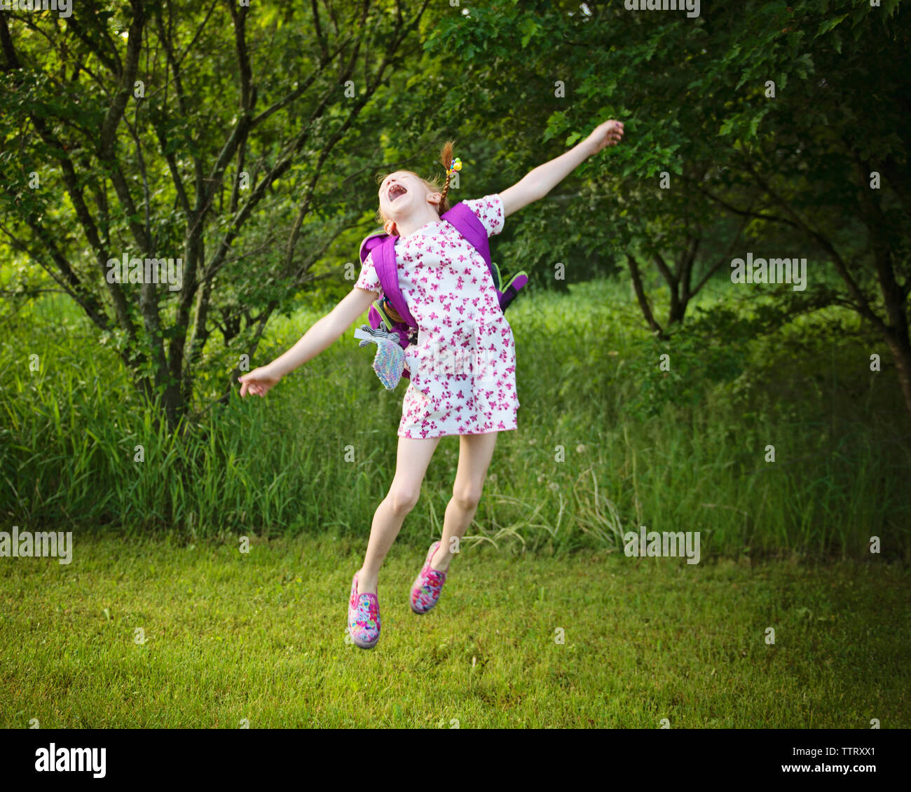 Allegro ragazza con zaino saltando su campo erboso a park Foto Stock