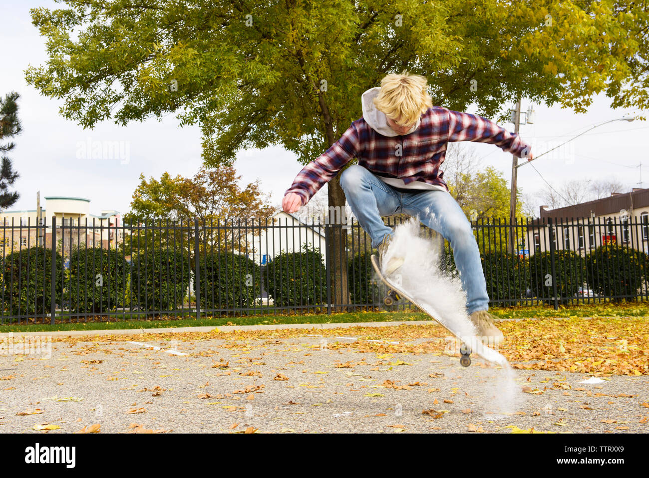 Uomo con vernice a polvere lo skateboard al parco durante l'autunno Foto Stock