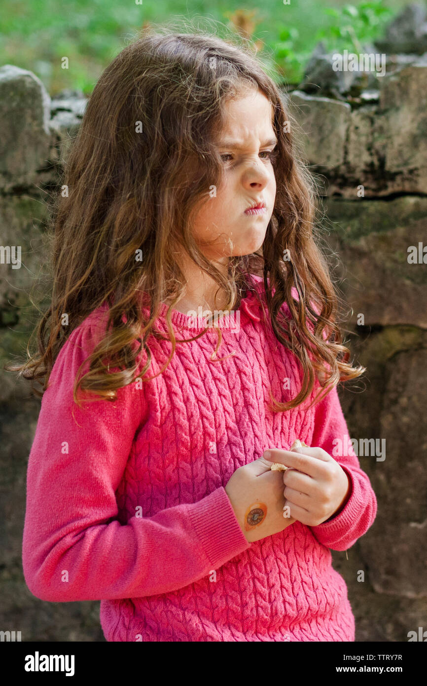 Arrabbiato scowling ragazza mentre in piedi contro il muro di pietra Foto Stock