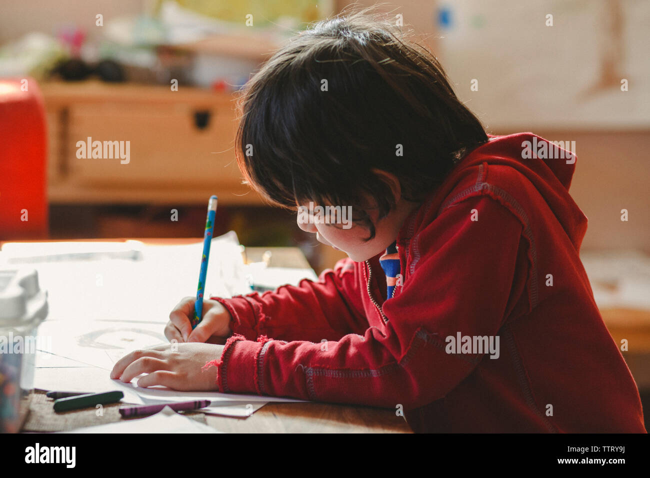 Vista laterale del ragazzo disegno sulla carta mentre è seduto a casa Foto Stock