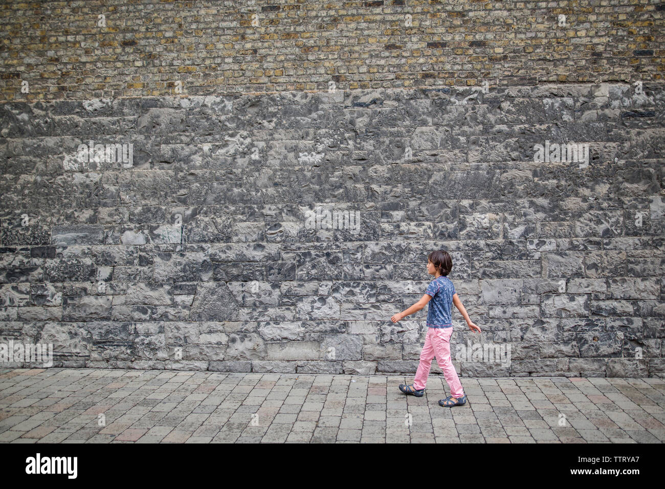 Vista laterale del ragazzo a piedi di marciapiede da muro di pietra nella città Foto Stock