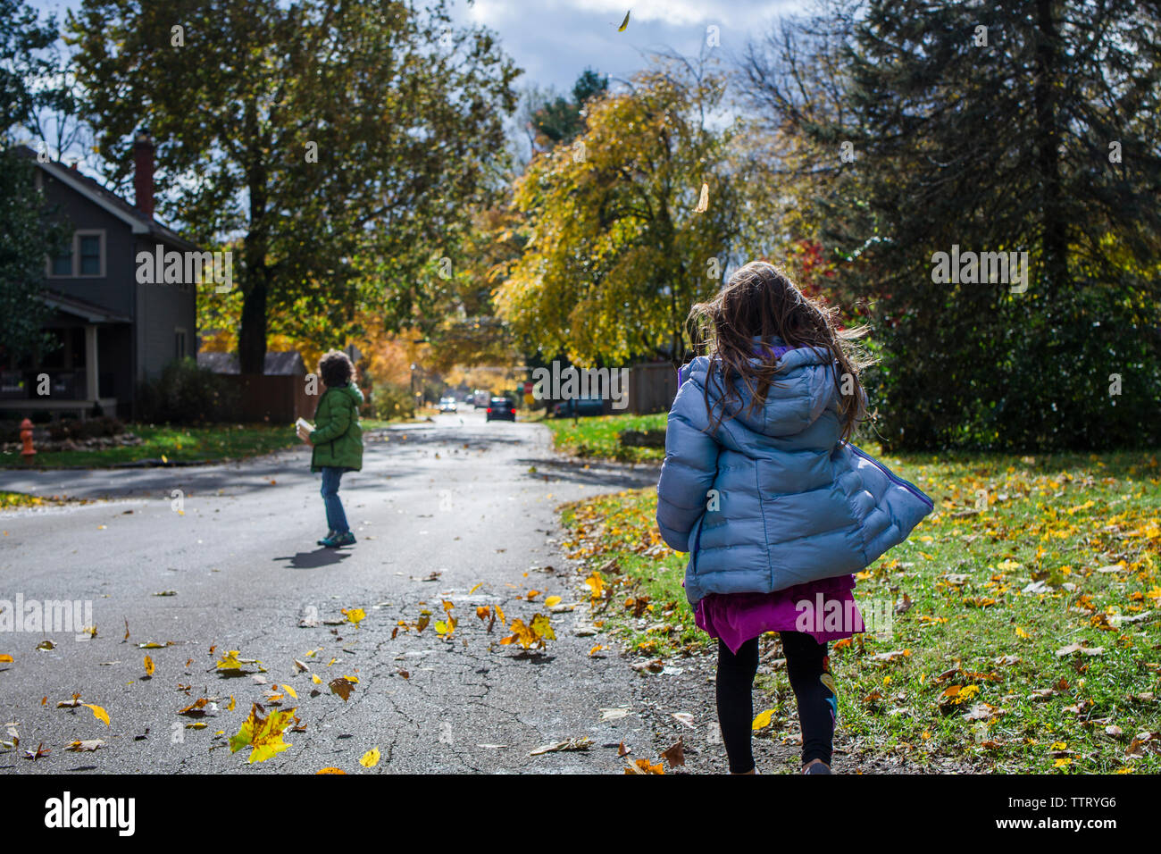 Due bambini di camminare insieme per la strada in mezzo alle foglie di soffiatura Foto Stock