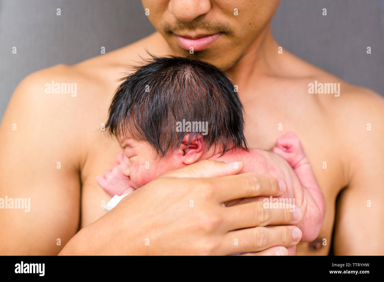 Vista frontale di un padre tenendo il suo neonato nelle sue braccia pelle a pelle Foto Stock