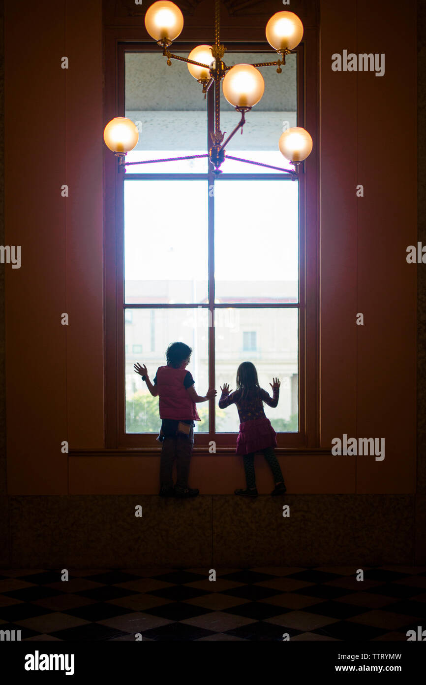 Silhouette di due bambini che guardano da una finestra di grandi dimensioni Foto Stock