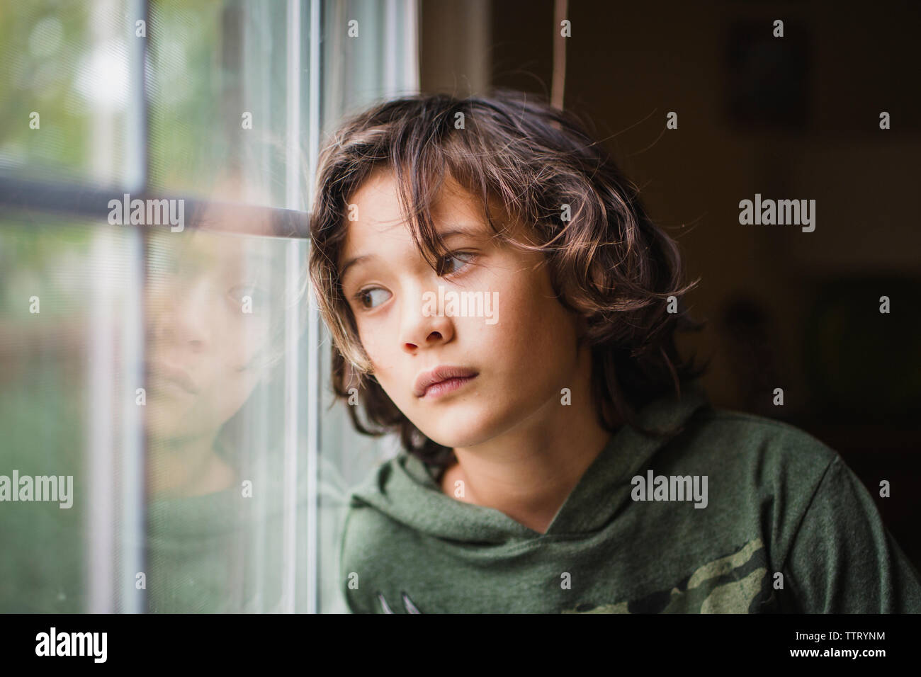 Un ragazzo sguardi fuori una finestra con espressione seria sul suo volto Foto Stock