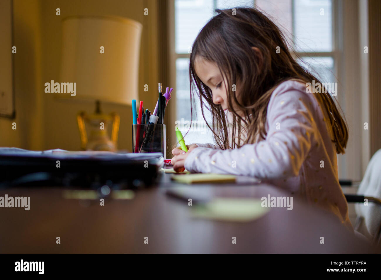 Una piccola ragazza studiare a una scrivania a casa Foto Stock