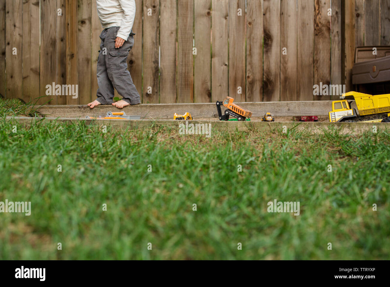 La metà inferiore di un ragazzo a piedi nudi a giocare con i giocattoli fuori Foto Stock