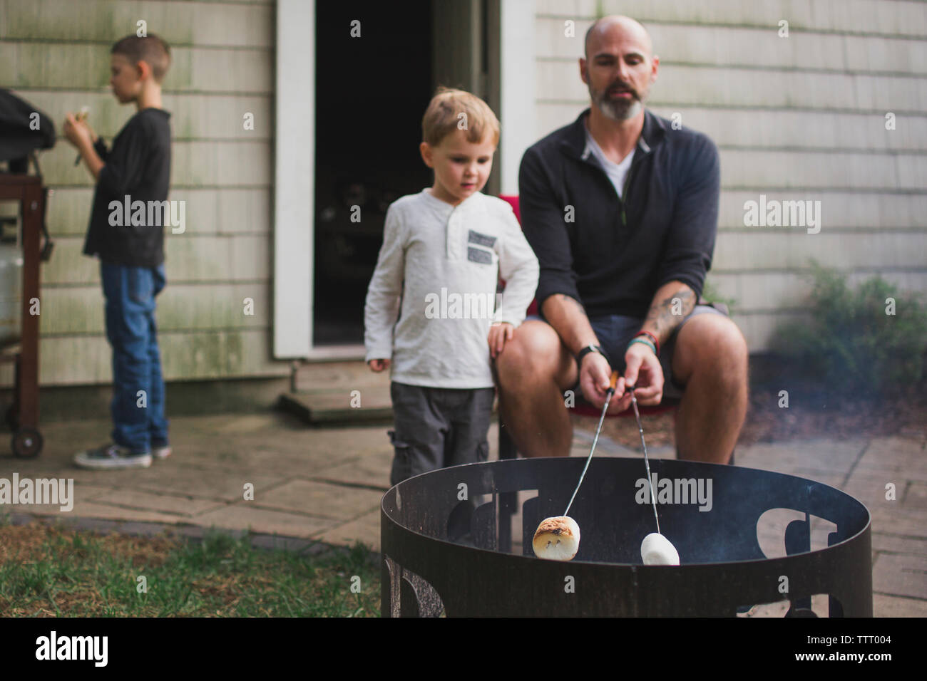 Un padre arrosti marshmallows con i suoi figli su una buca per il fuoco Foto Stock