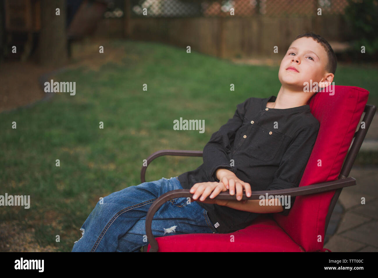 Un giovane ragazzo seduto da solo in una sedia con un look sognante Foto Stock