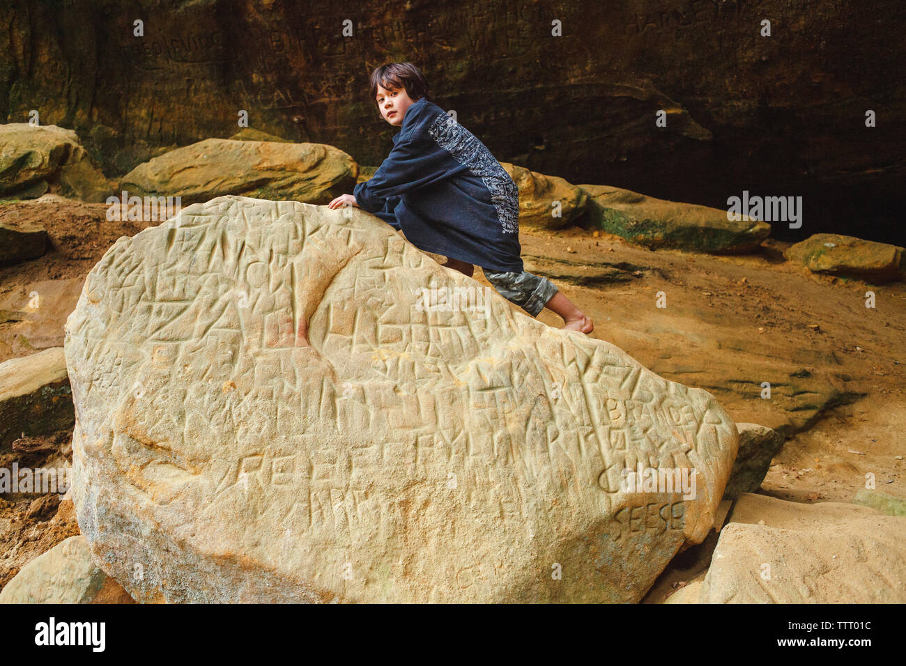 Ritratto di un piccolo ragazzo a piedi nudi arrampicata su roccia di grandi dimensioni in un soleggiato gorge Foto Stock