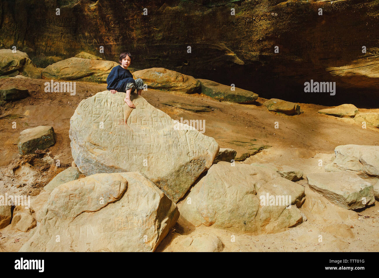 Un piccolo ragazzo si siede a piedi nudi su una roccia d'oro circondato da pareti di roccia Foto Stock
