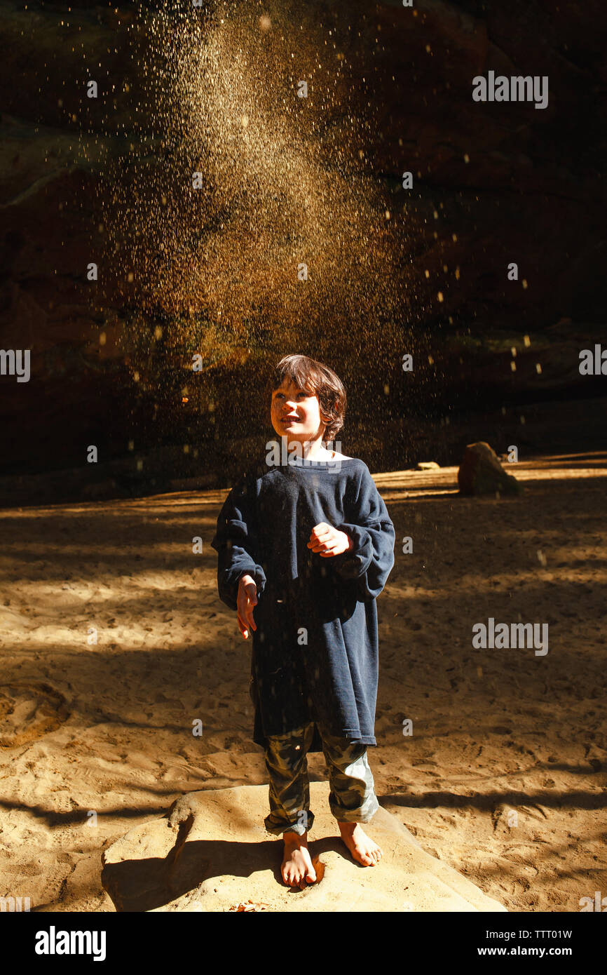 Un piccolo bambino a piedi nudi getta sabbia dorata in aria in gola soleggiato Foto Stock