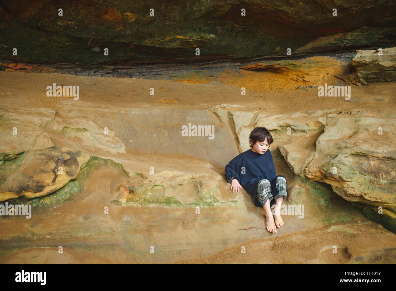 Un bambino piccolo si siede a piedi nudi cullati sulla rocciosa battuta di arenaria nella gola Foto Stock