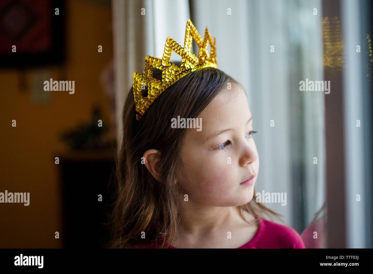 Ritratto di grave bambina in una corona d'oro a guardare fuori dalla finestra Foto Stock