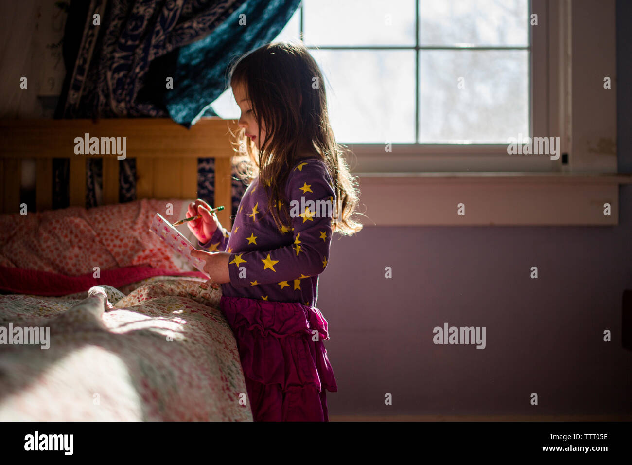 Una piccola ragazza sorge nella patch di luce nella camera da letto iscritto nel journal Foto Stock