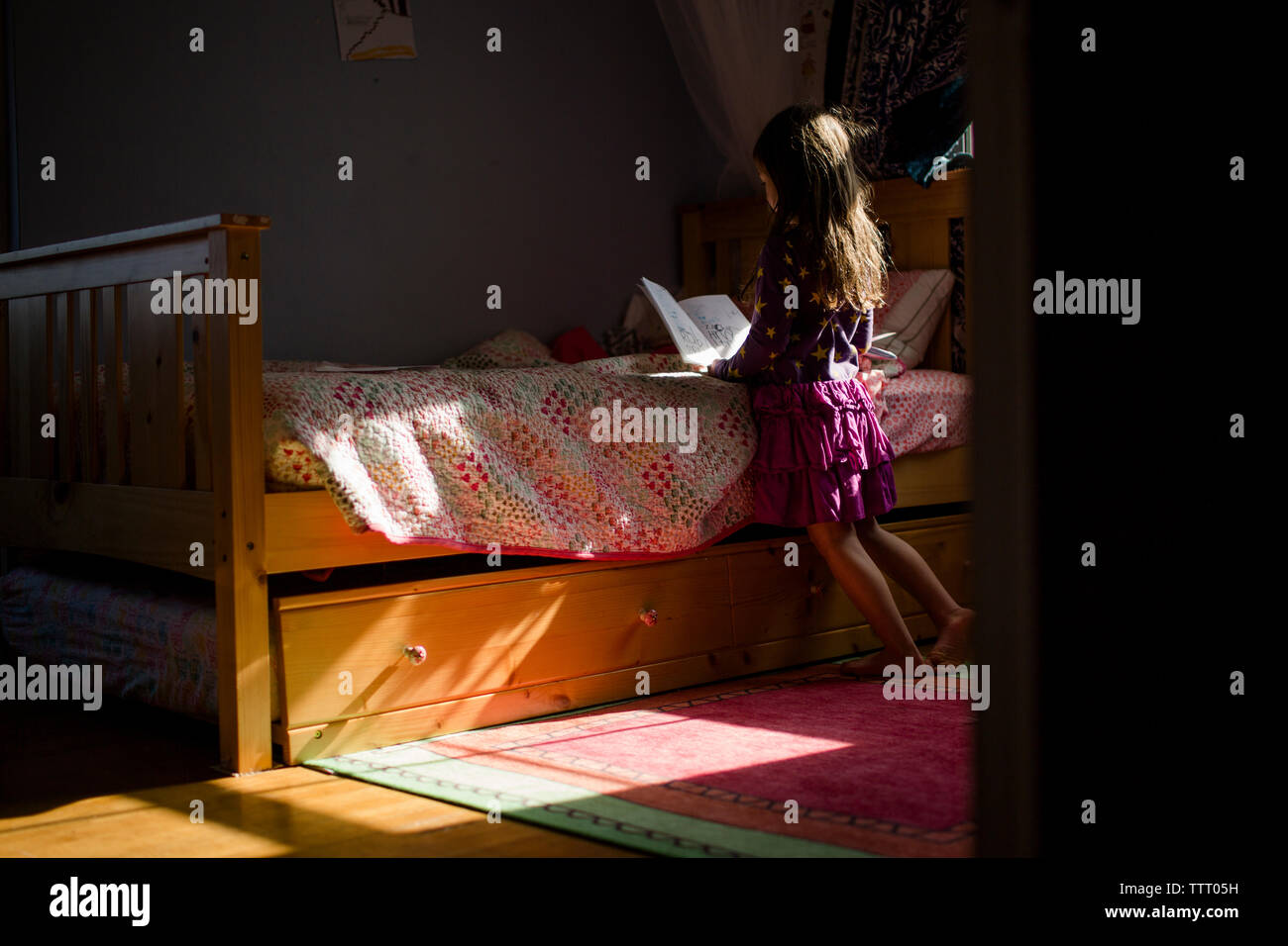 Vista posteriore di una piccola ragazza leggendo un libro da sola nella sua camera da letto Foto Stock