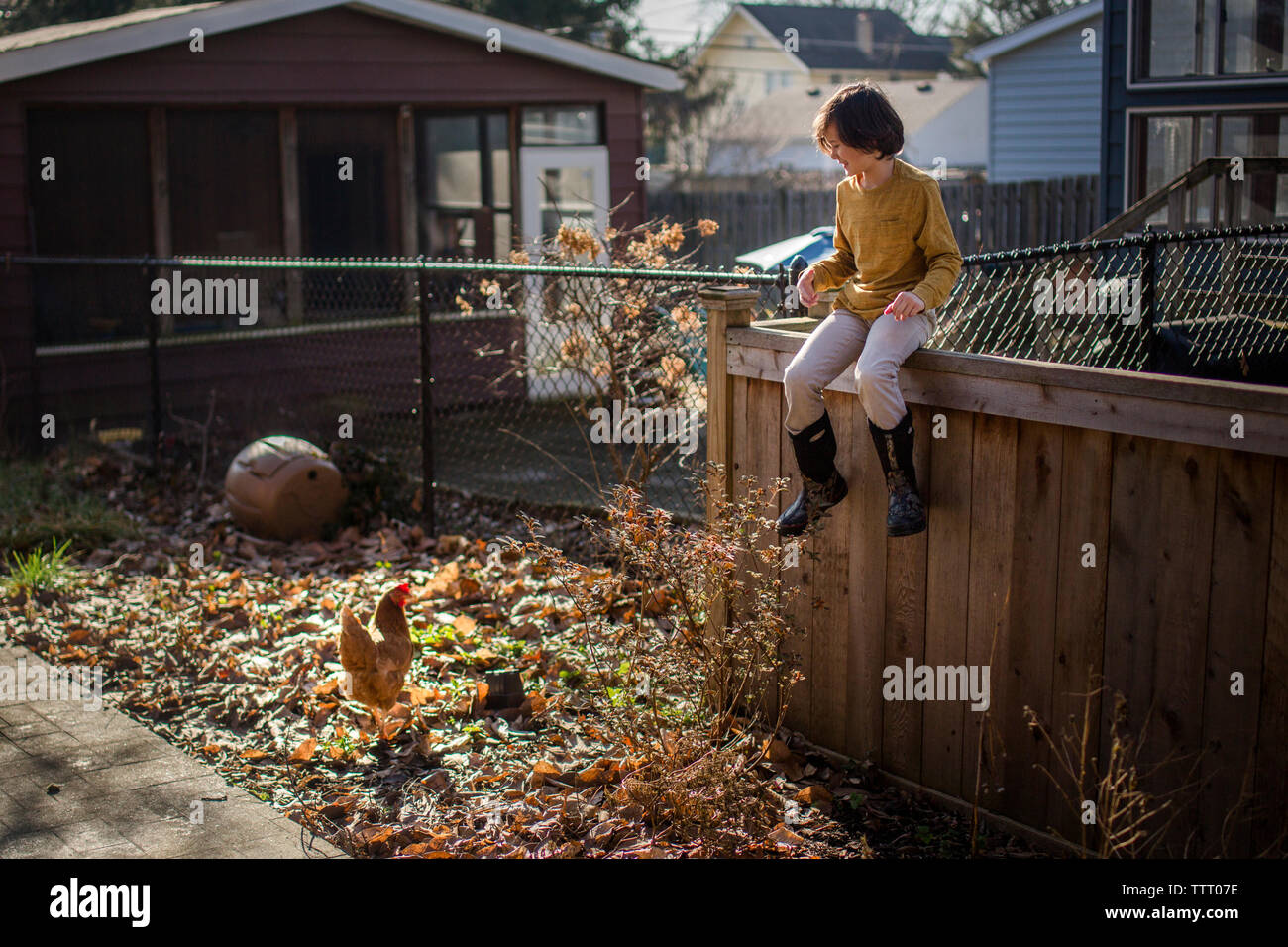 Un bambino felice in giallo si siede su un cortile recinto sorridente a un pollo Foto Stock