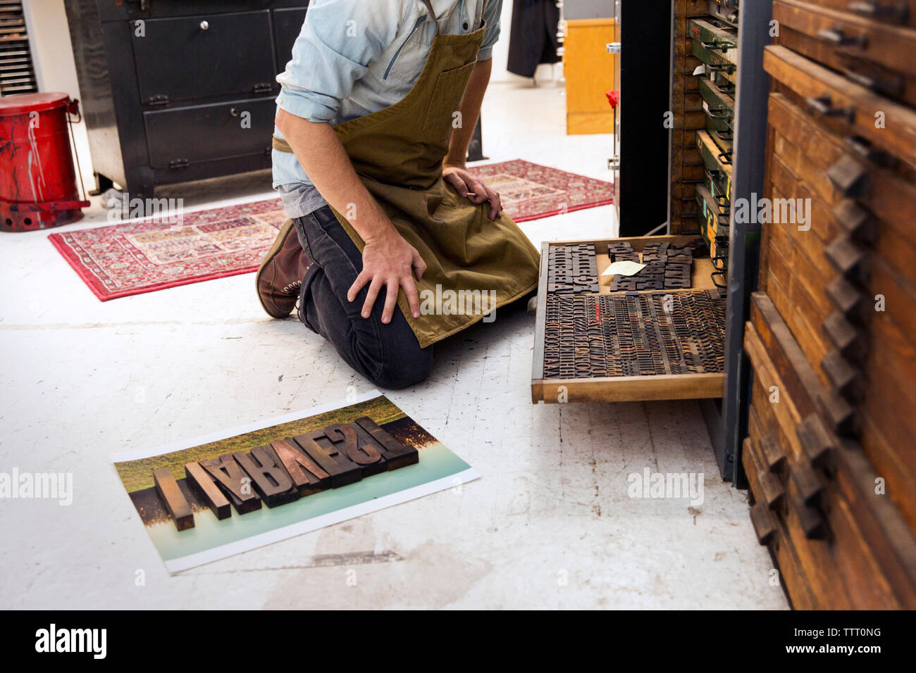 Sezione bassa dell'uomo con alfabeti di legno nella macchina da stampa Foto Stock