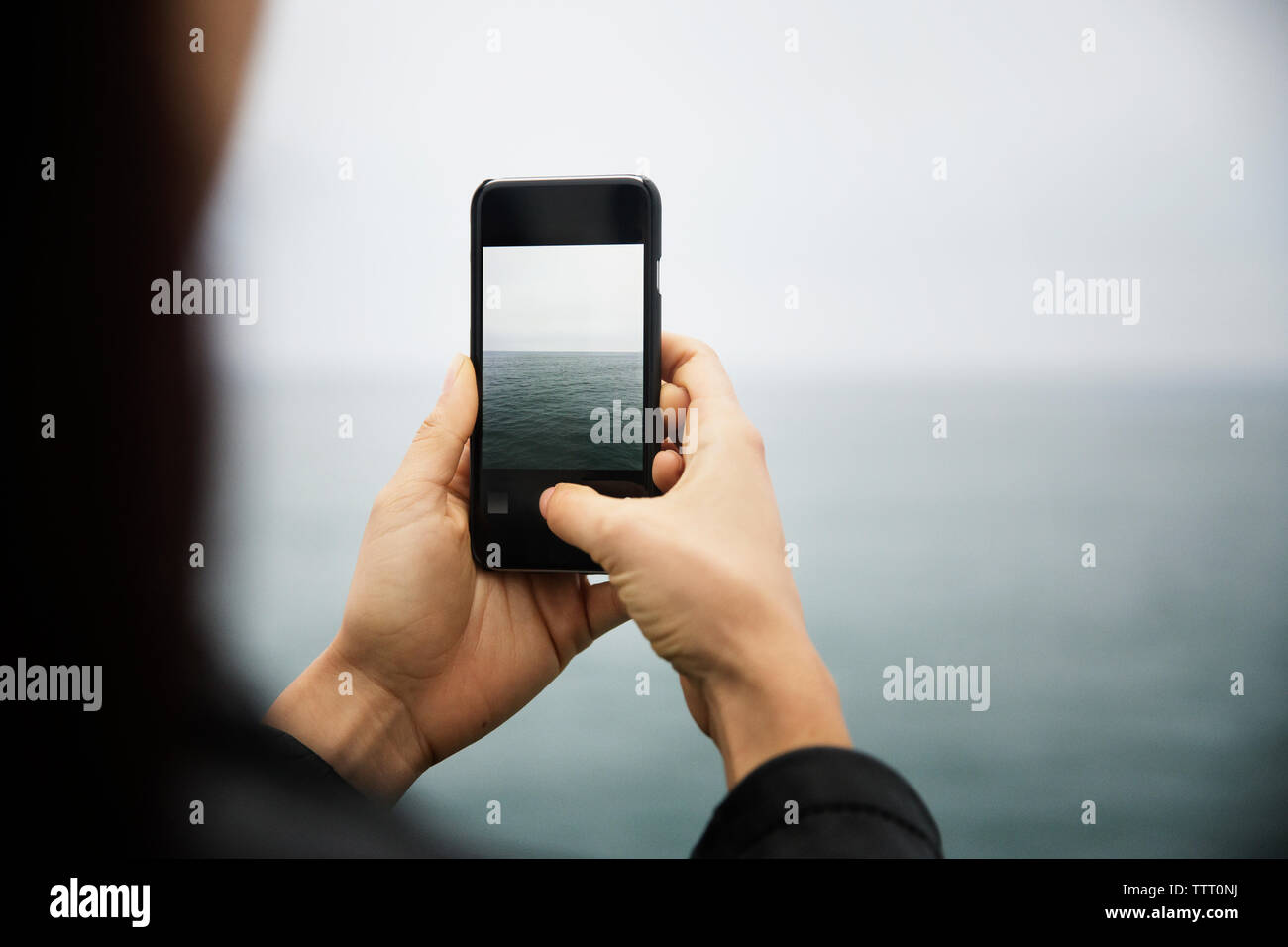 Immagine ritagliata della donna fotografare mare attraverso il telefono cellulare Foto Stock