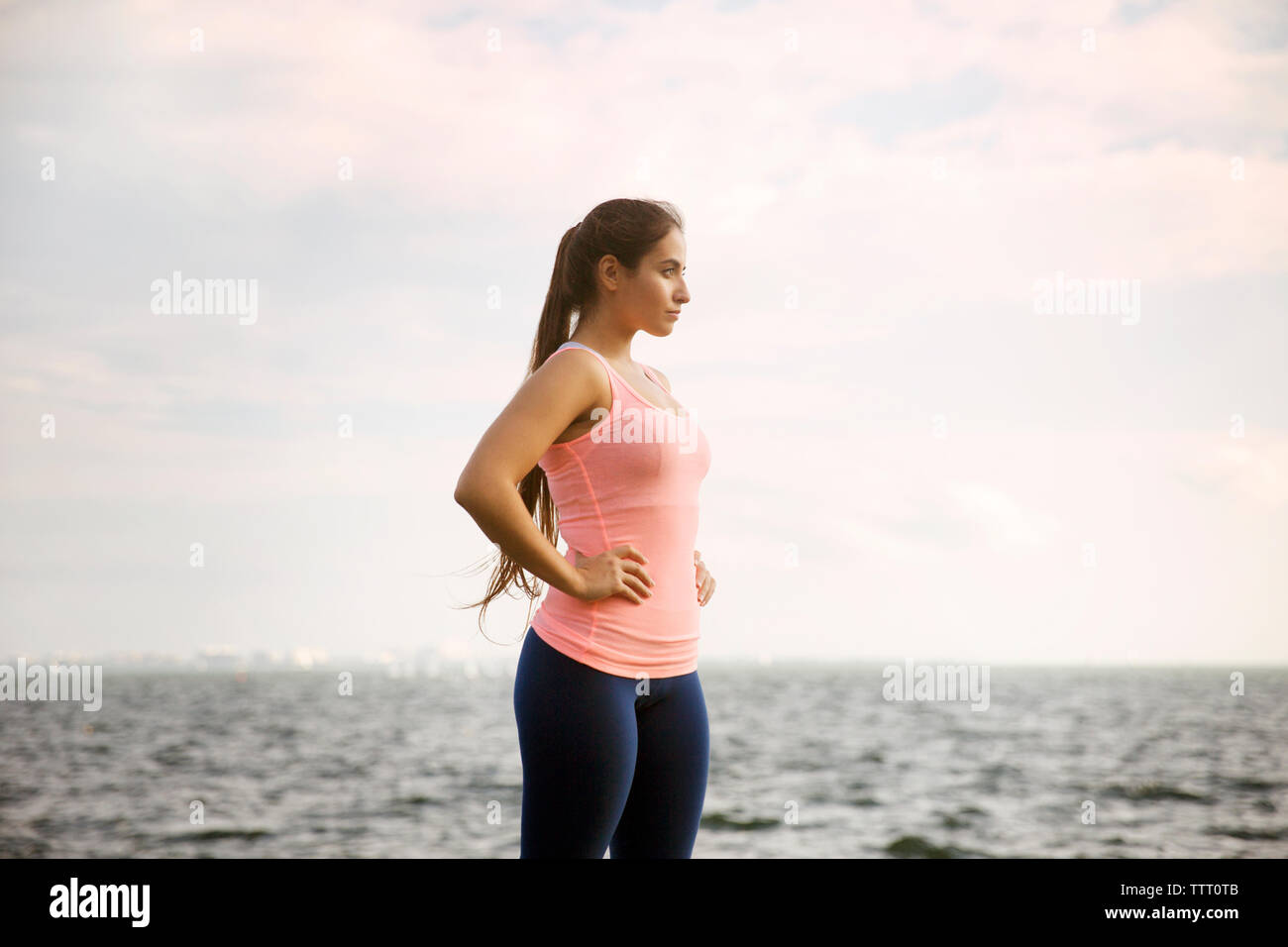 Vista laterale della donna in piedi con le mani sui hip contro il mare e il cielo Foto Stock