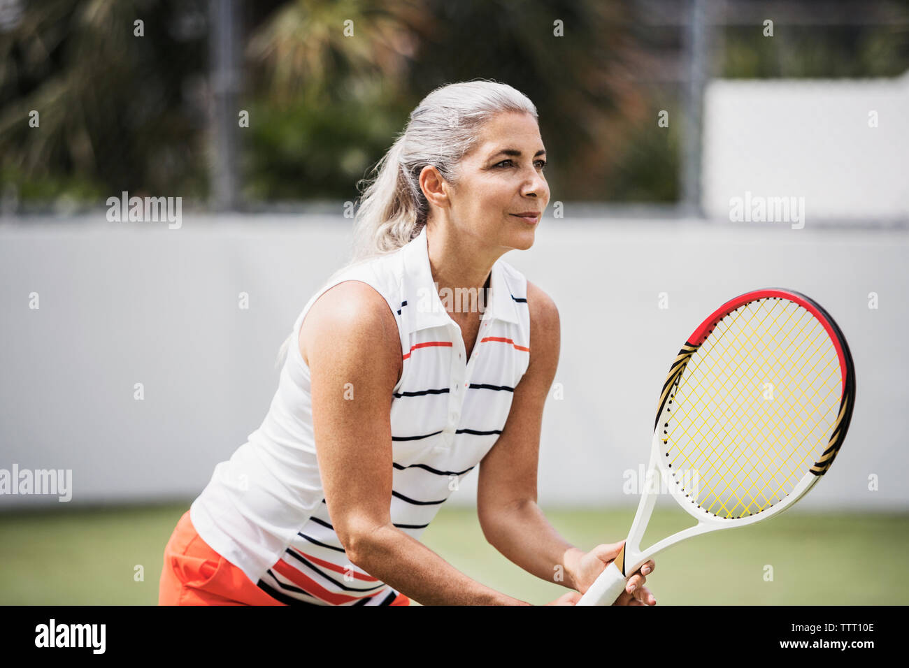 Determinata donna matura giocando a tennis su corte Foto Stock
