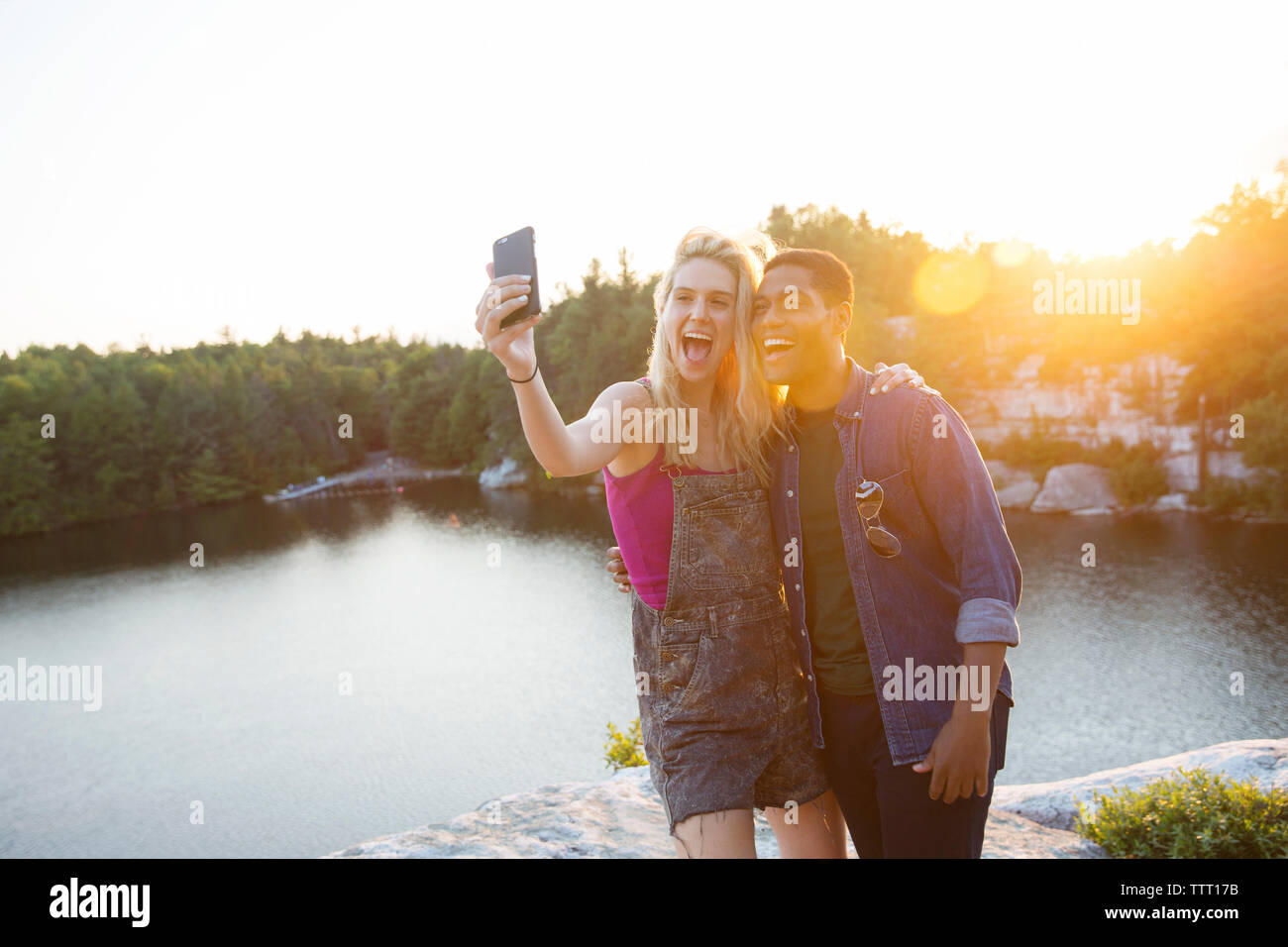 Allegro amici prendendo selfie attraverso la telecamera dal lago durante il tramonto Foto Stock