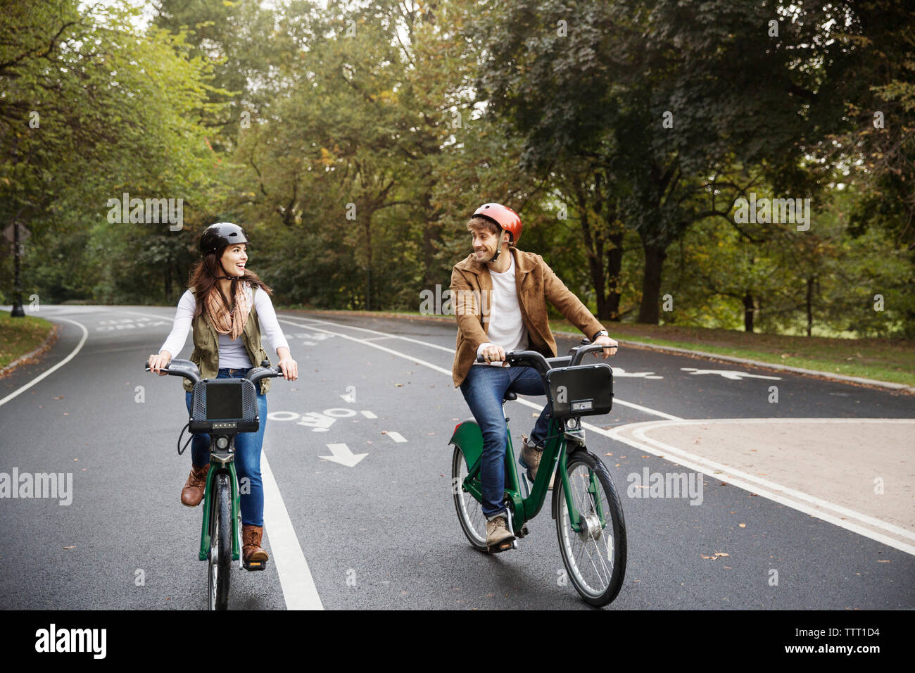 Coppia sorridente equitazione bicicletta su strada in posizione di parcheggio Foto Stock