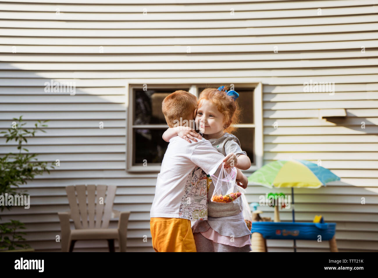 Carino bambini abbracciando mantenendo i sacchetti di cioccolato contro la casa Foto Stock