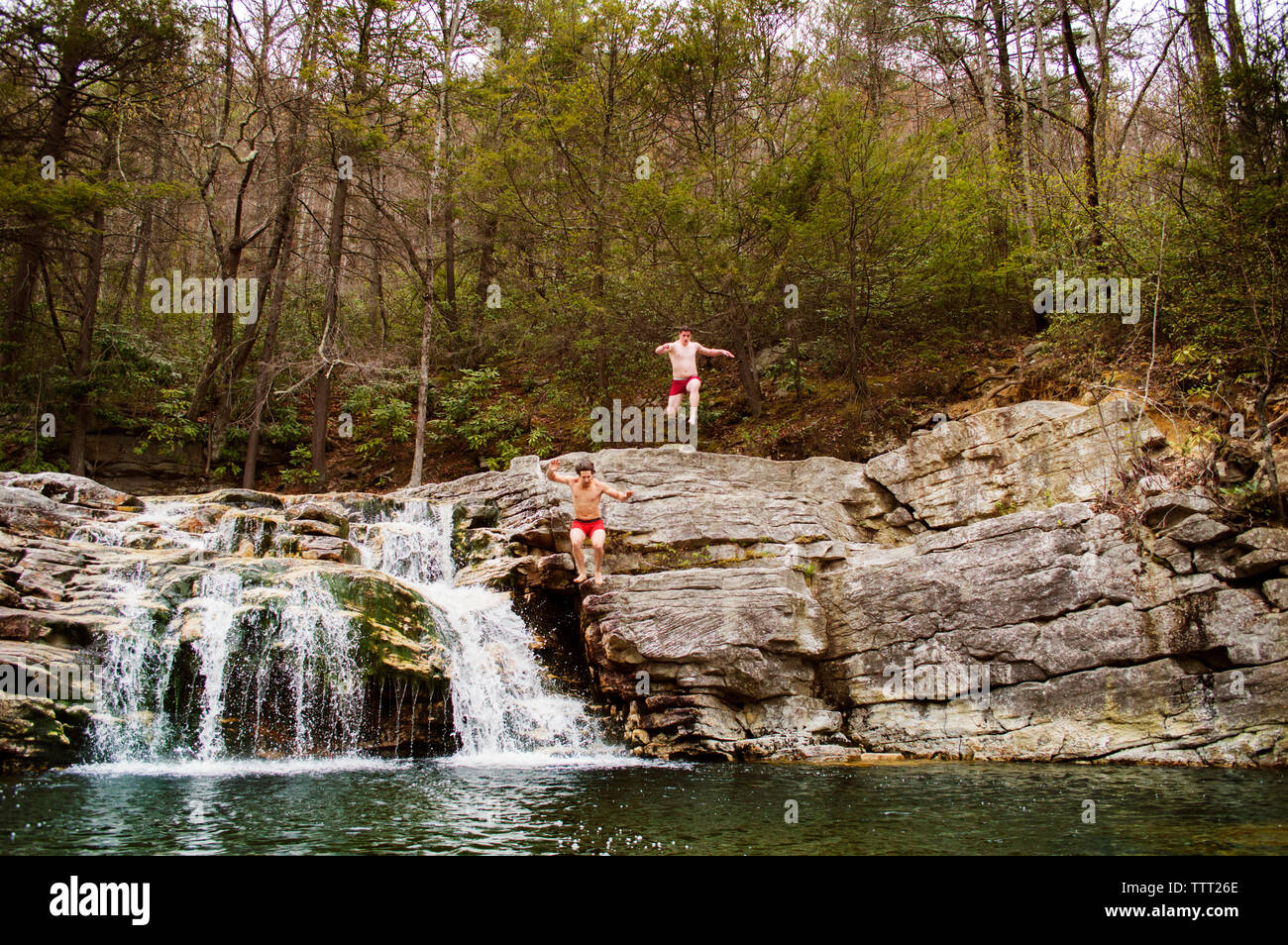Amici di sesso maschile il salto nel lago contro la scogliera rocciosa dal bordo della foresta Foto Stock