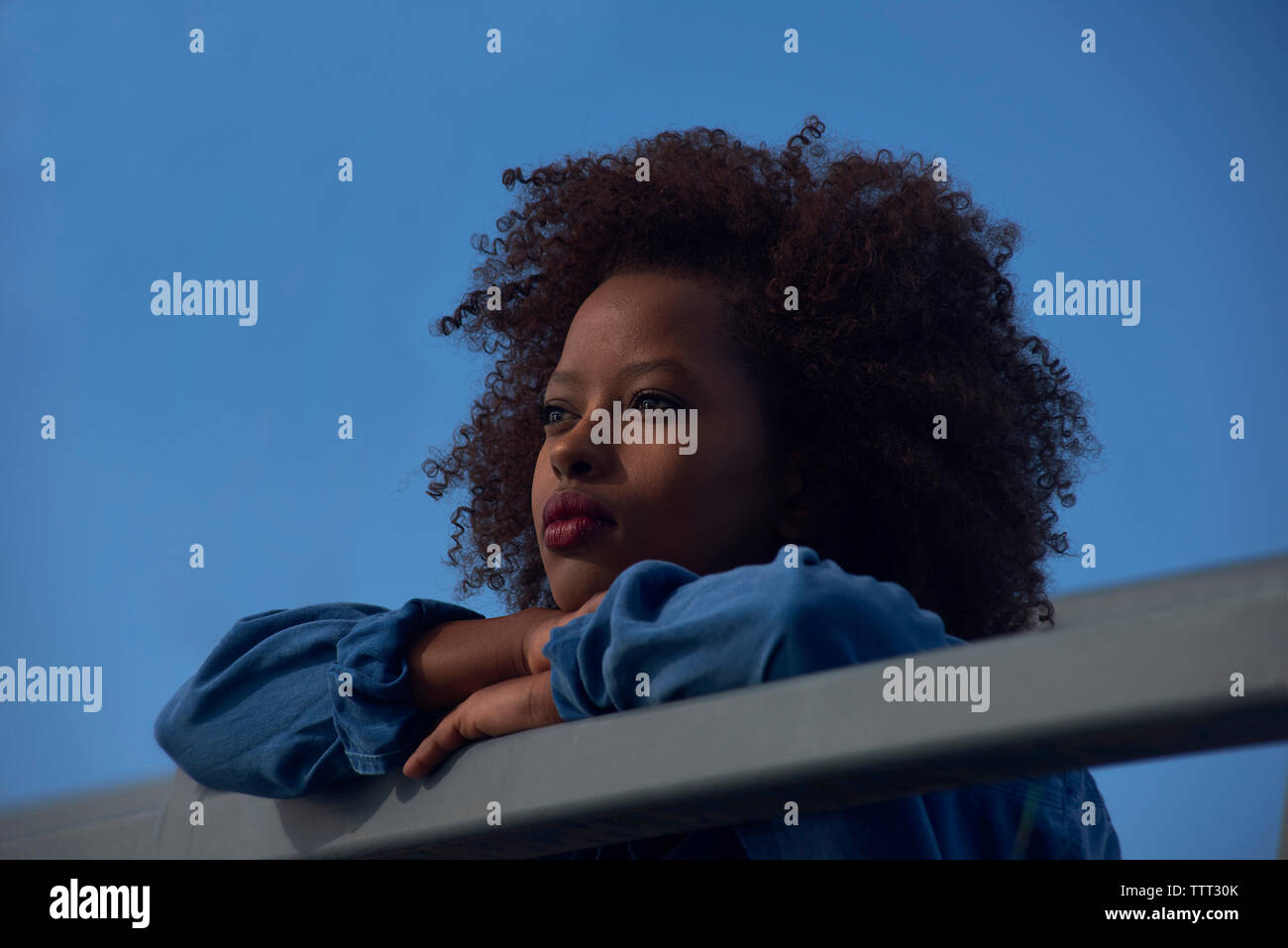 Basso angolo di vista premurosa donna appoggiata sulla ringhiera contro il cielo blu chiaro Foto Stock