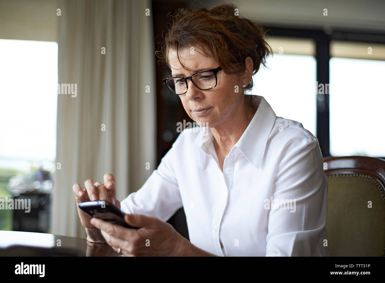 Donna che utilizza il cellulare mentre seduti a casa Foto Stock