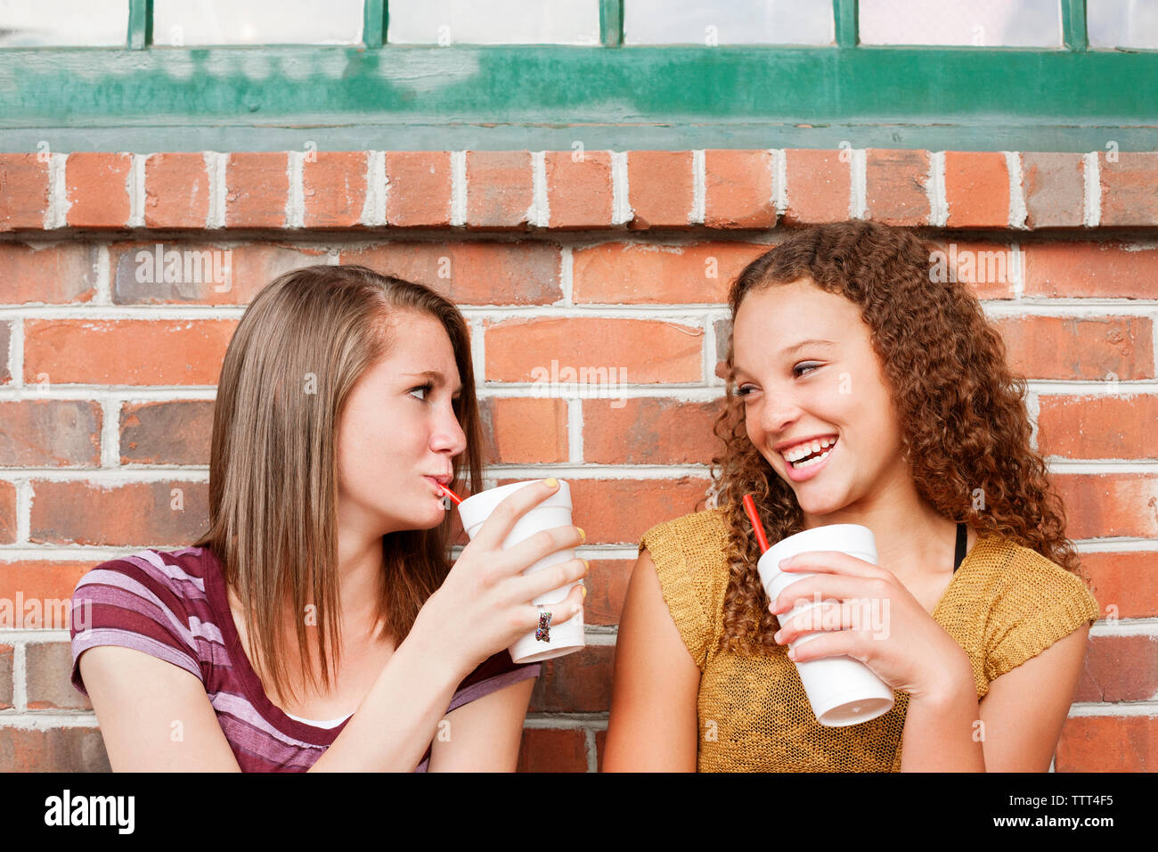 Gli amici sorseggiando drink seduto contro un muro di mattoni Foto Stock