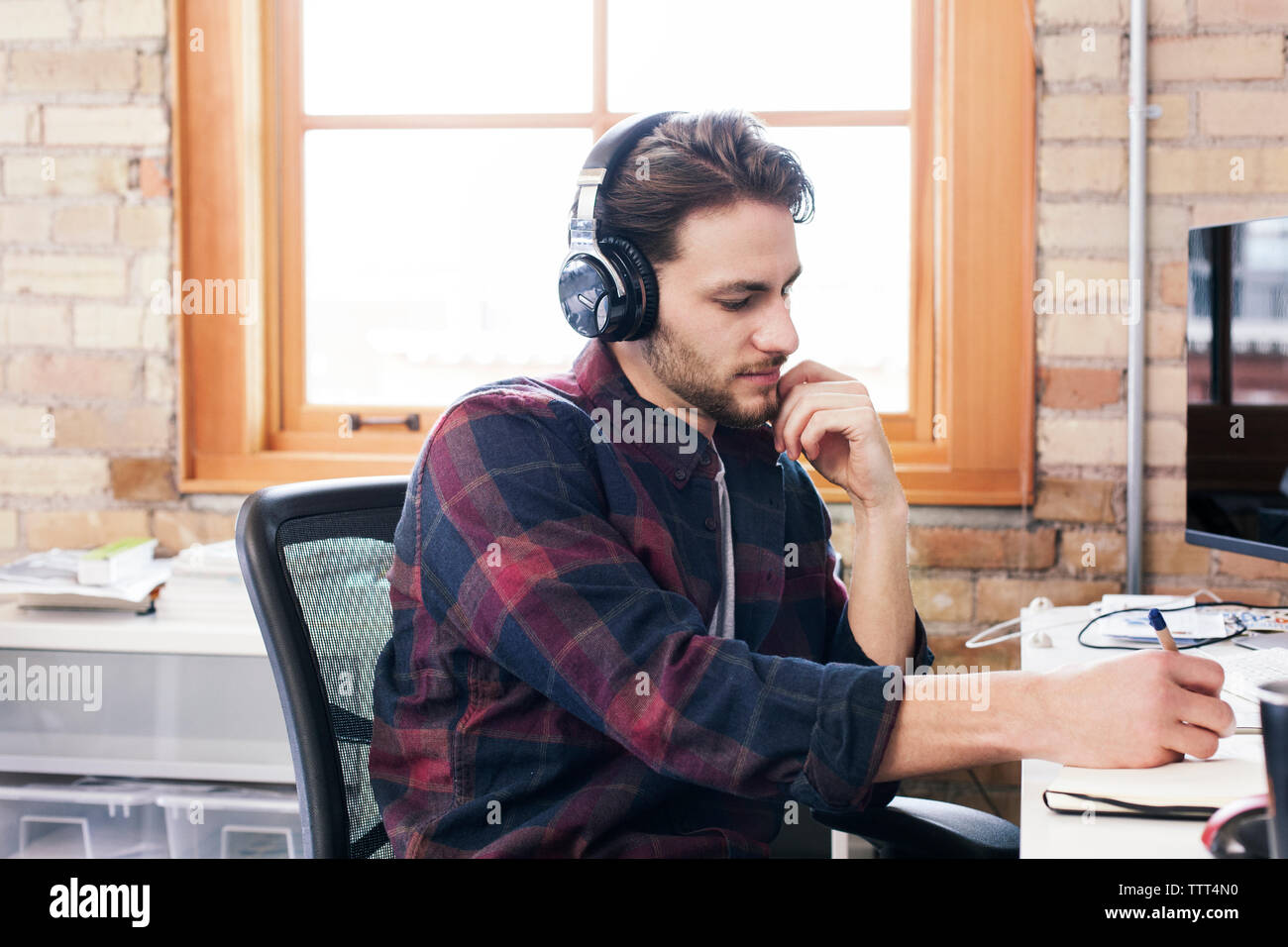 uomo d'affari che indossa le cuffie scrivendo sul diario mentre lavora in ufficio Foto Stock