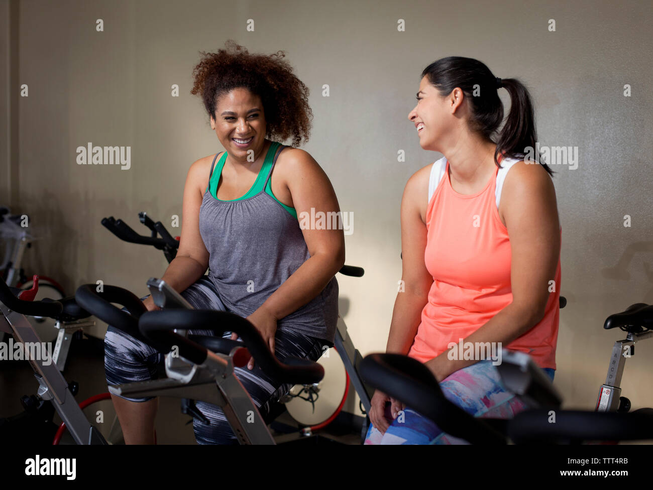 Happy amici di sesso femminile di parlare mentre è seduto sulla cyclette in palestra Foto Stock