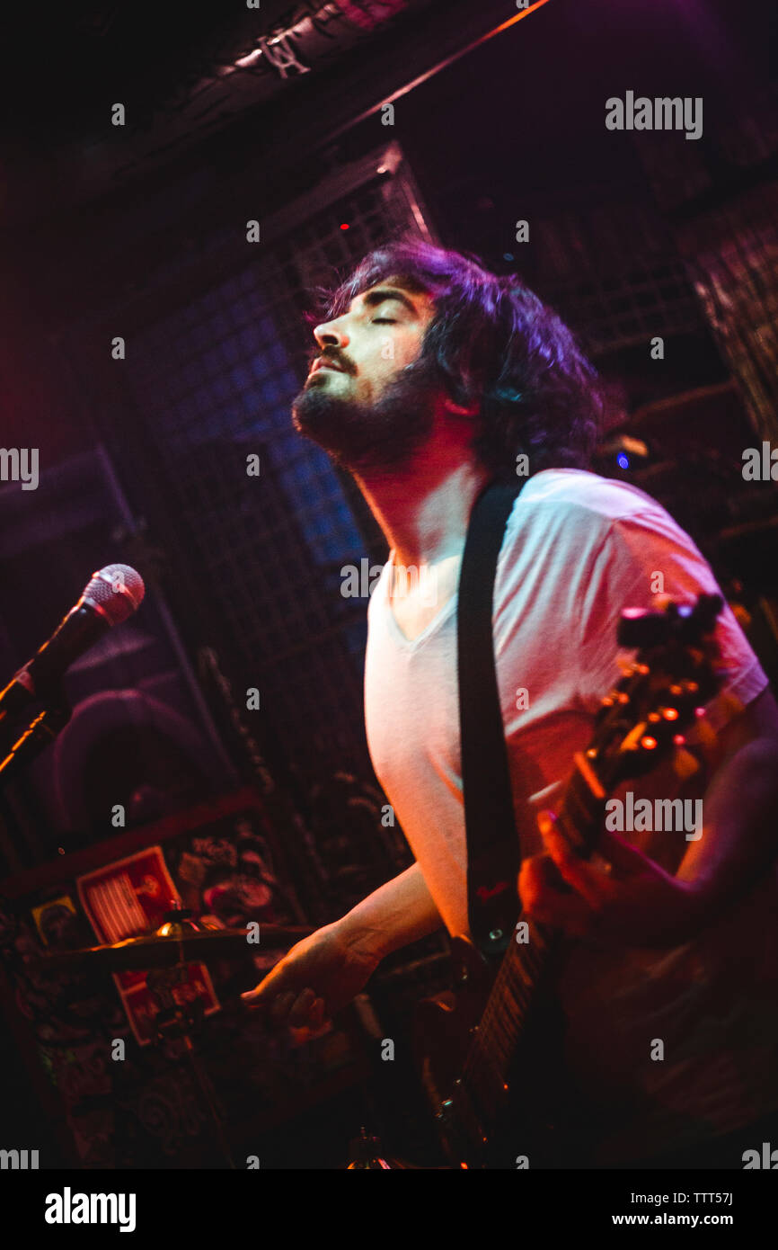 Uomo con gli occhi chiusi di cantare e suonare la chitarra in discoteca Foto Stock