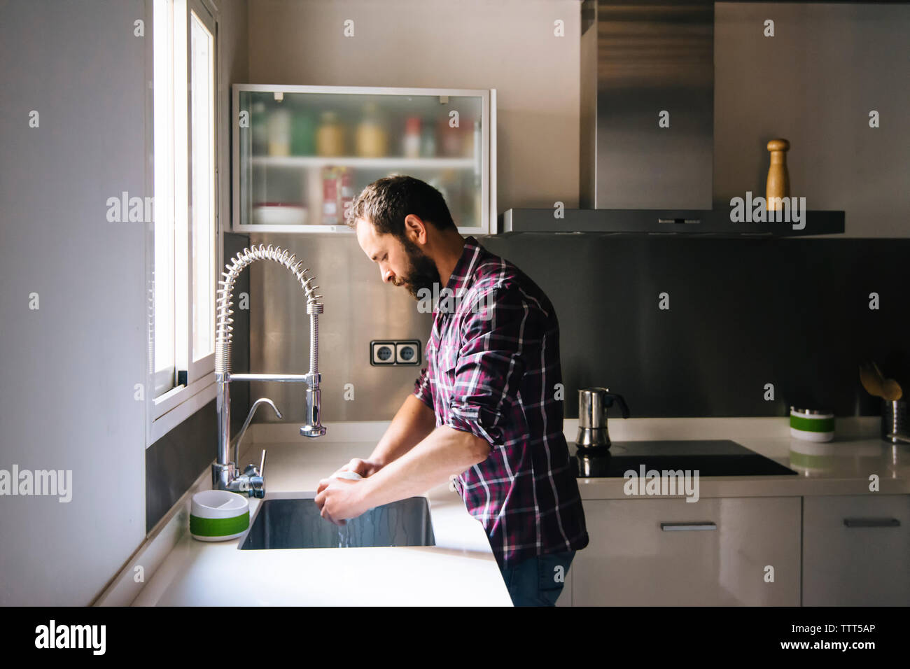 Uomo con la barba e plaid shirt lavaggio piatti a casa. Foto Stock