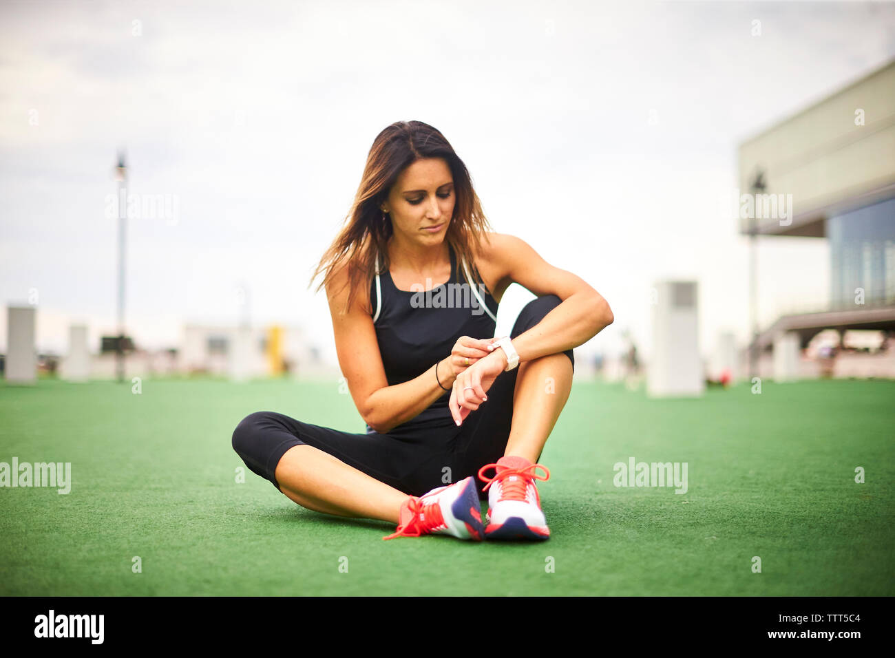 Un atletico donna seduta sul manto erboso controllando il suo orologio fitness. Foto Stock