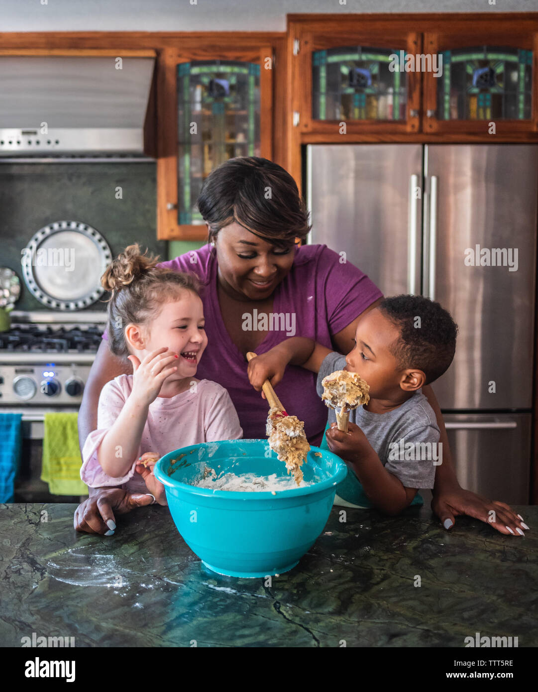 Madre sorridere mentre i bambini fanno i cookie insieme Foto Stock