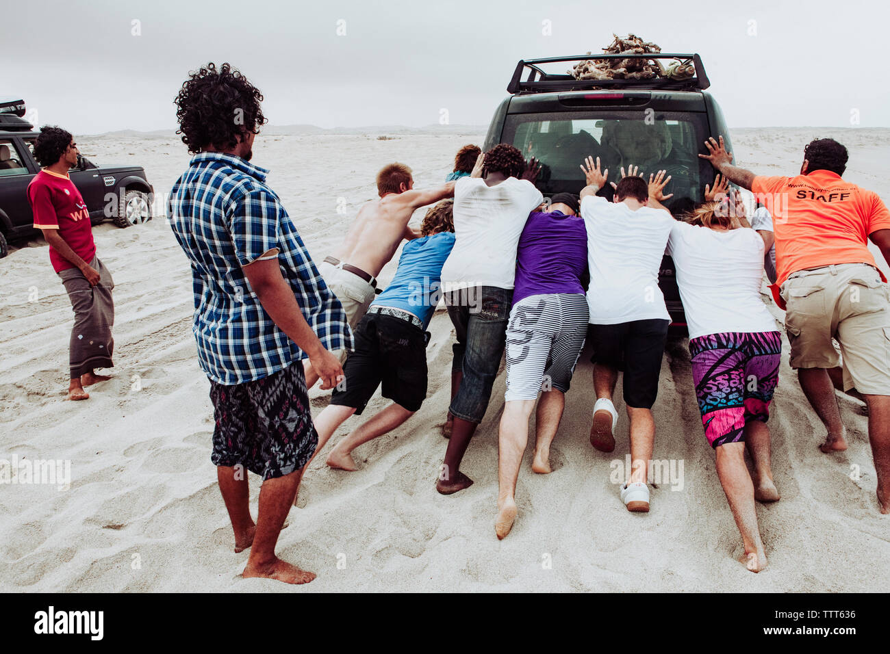 Un gruppo di uomini adulti il push di un veicolo fuoristrada bloccati nella sabbia, Oman Foto Stock