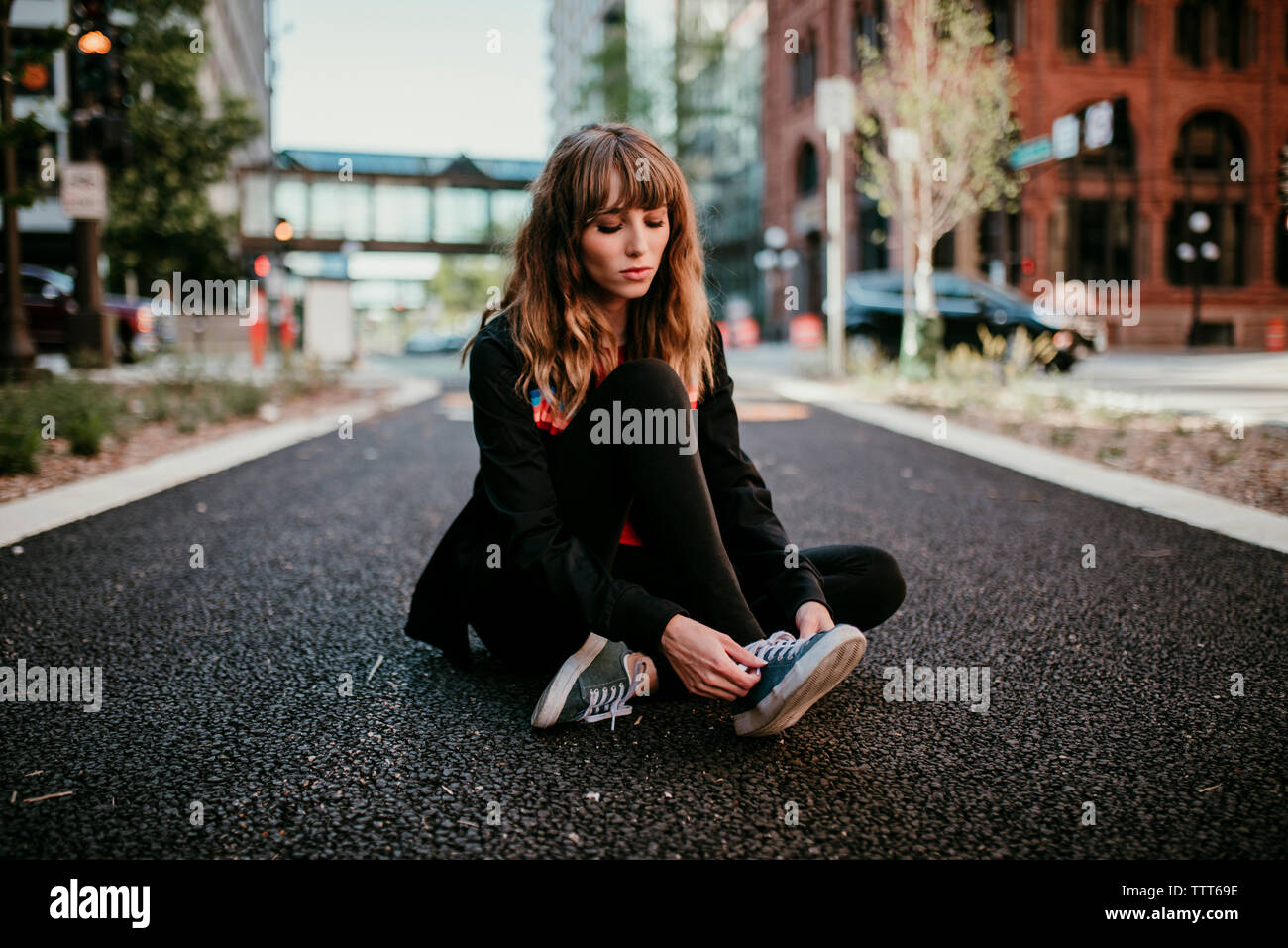 Giovane donna passalacci di legatura seduto su una strada di città Foto Stock