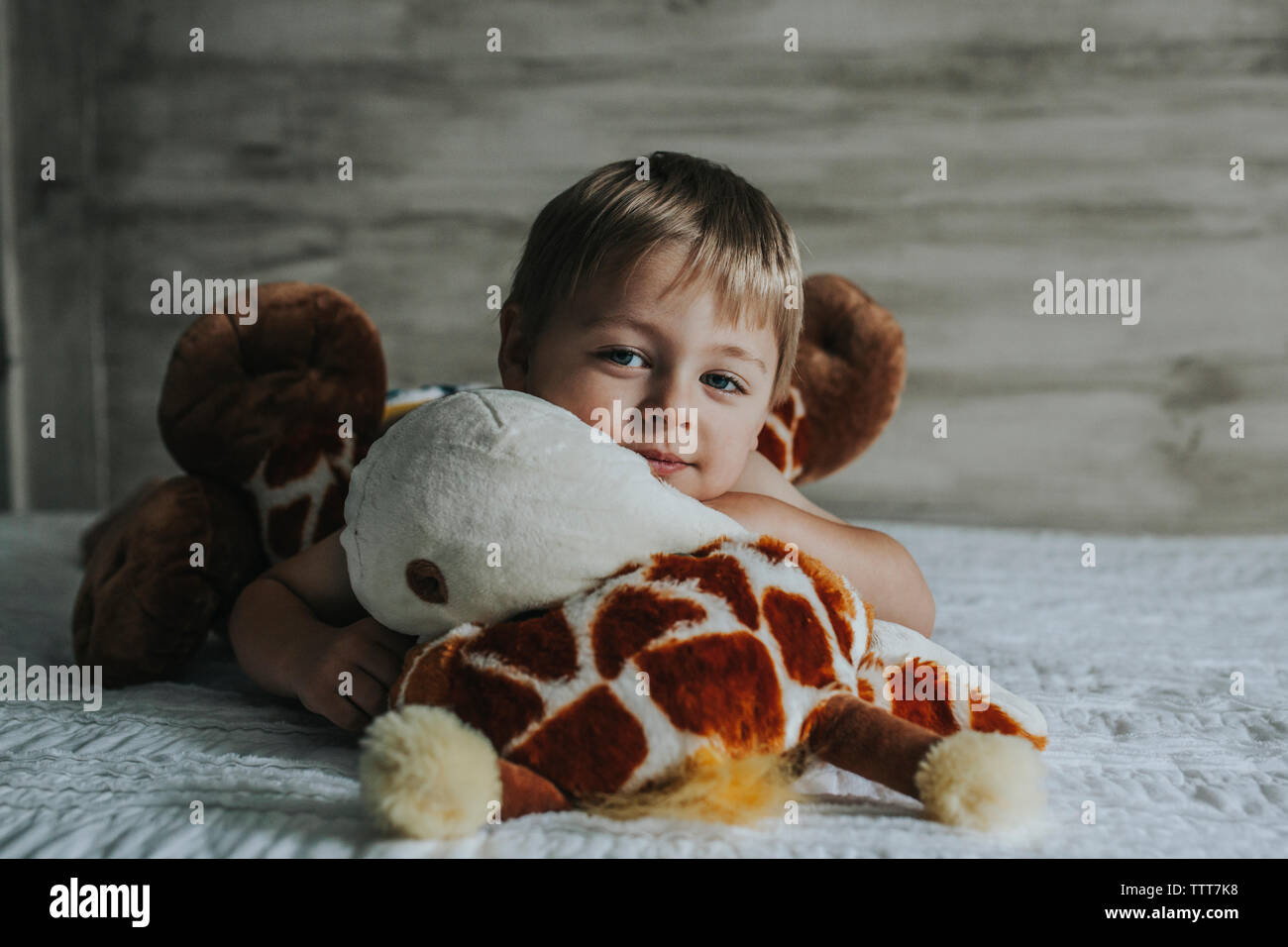 Ritratto di ragazzo giocando con i giocattoli imbottiti su letto di casa Foto Stock