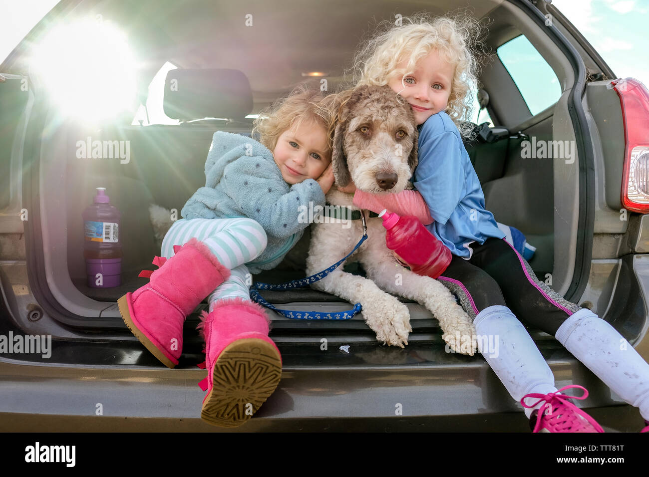 Ritratto di sorridere sorelle abbracciando dog sitter nel baule auto Foto Stock