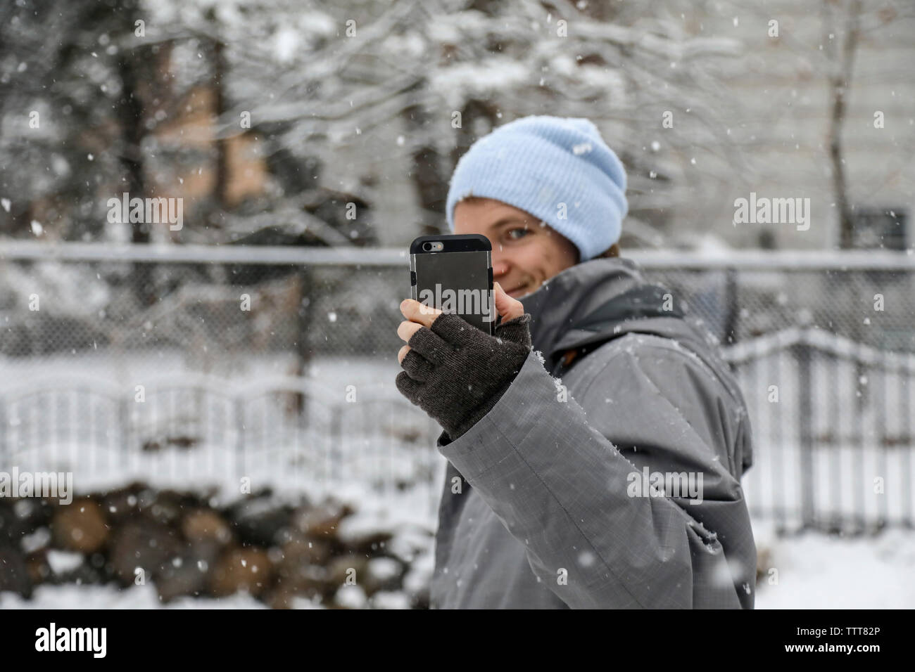 Uomo di indossare un abbigliamento caldo durante l'assunzione di selfie con smart phone durante la nevicata Foto Stock
