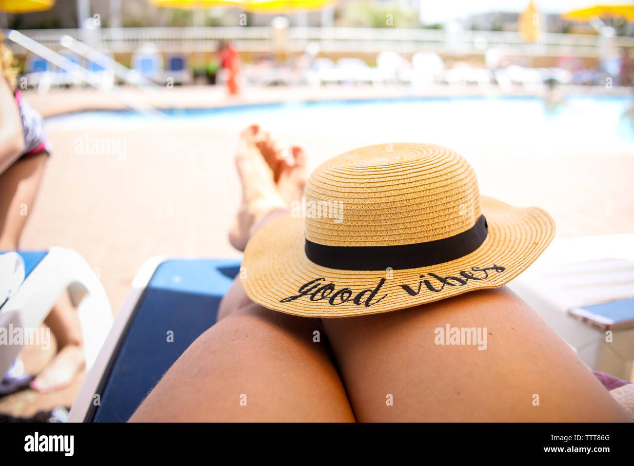 Good Vibes cappello di paglia sulle gambe seduti in piscina nella luce del sole Foto Stock