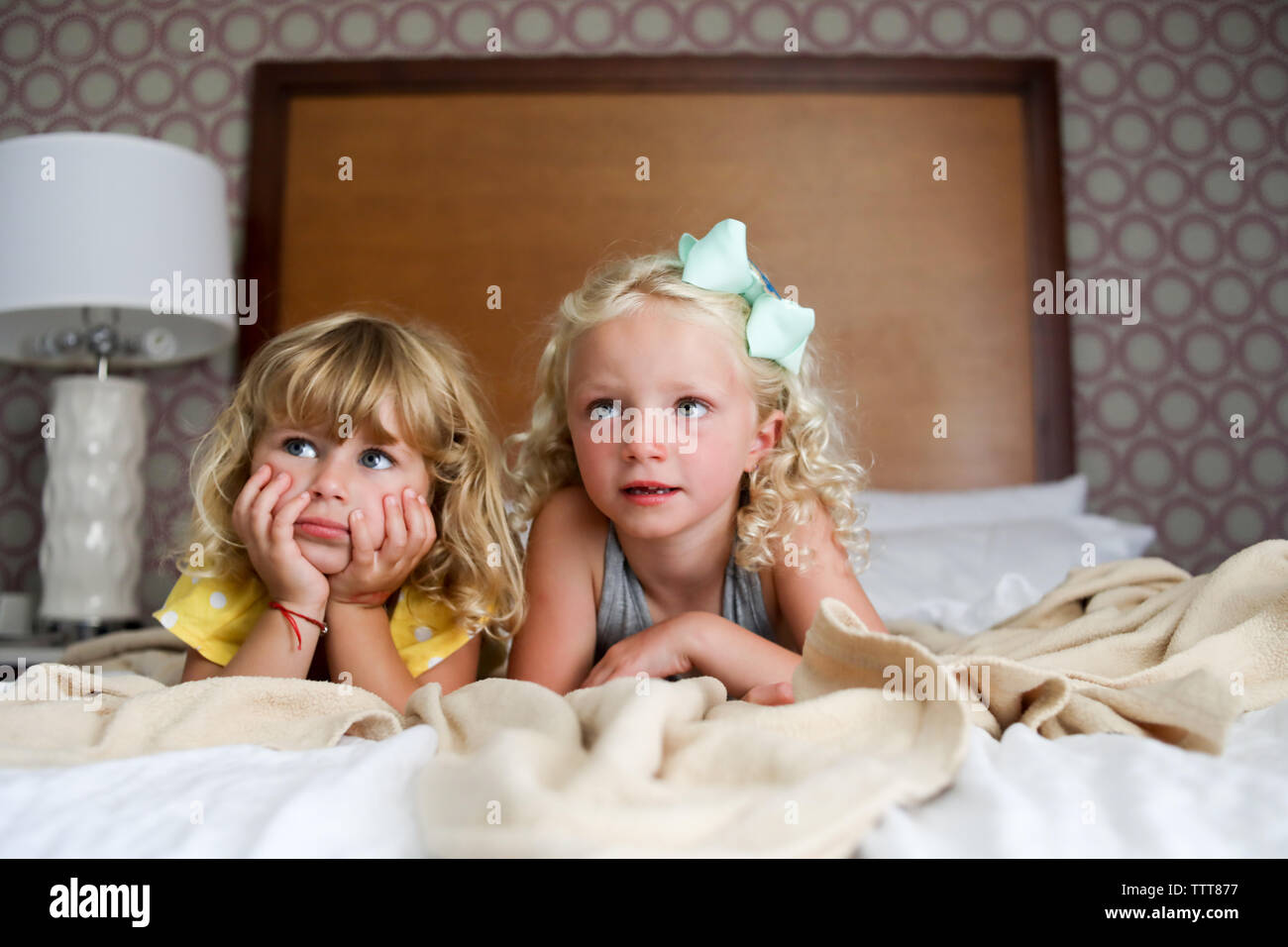 Due ragazze sul letto disfatto guardando la tv le mani sul viso Foto Stock